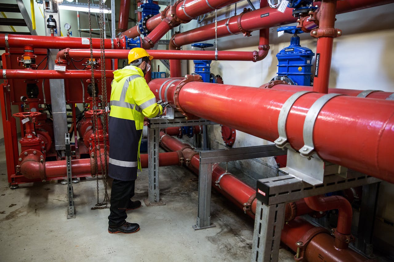 about-bg Engineer with safety gear inspecting red industrial piping system indoors.