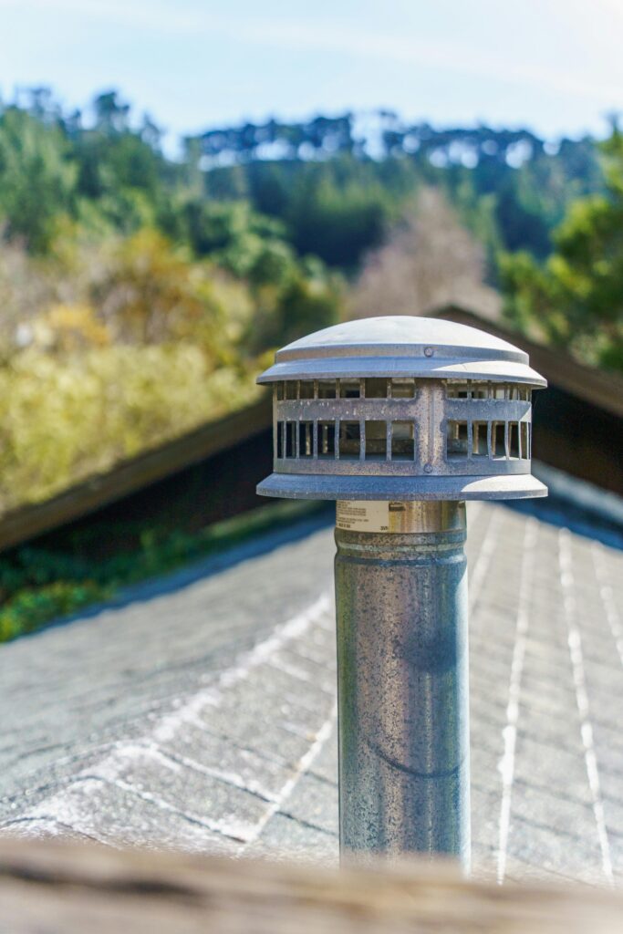 Close-up of a chimney vent on a rooftop against a forested background, capturing outdoor tranquility.